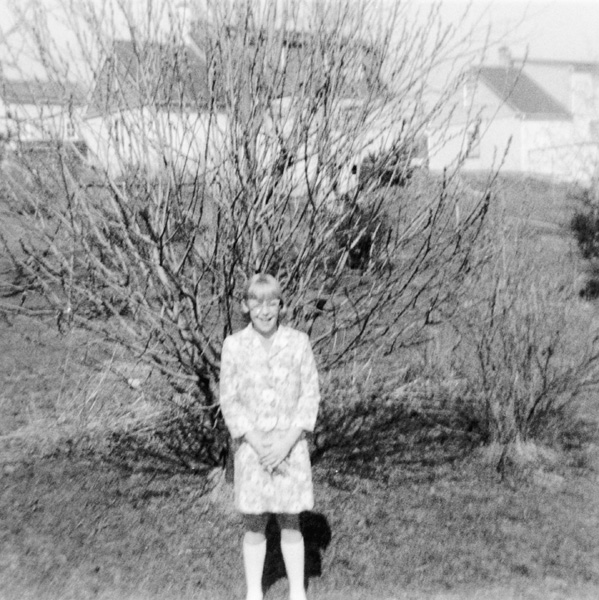 My sister Kay in front of the unbloomed forsythia, c. 1966.