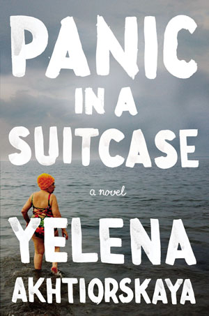 Panic in a Suitcase cover art. Large white text in front of a woman standing in front of the sea