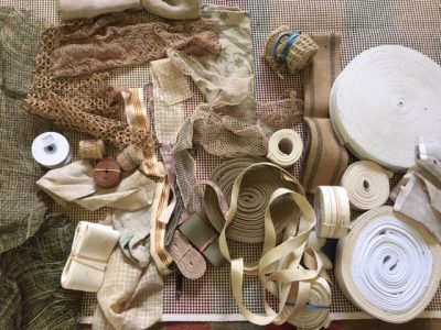 Flat-lay photo of white, brown, and cream-colored crafting supplies including fabric and ribbon