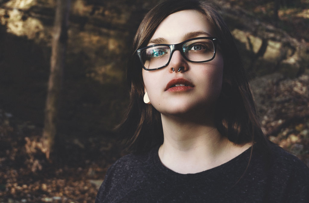 woman wearing glasses looking into distance against dark, wooded background