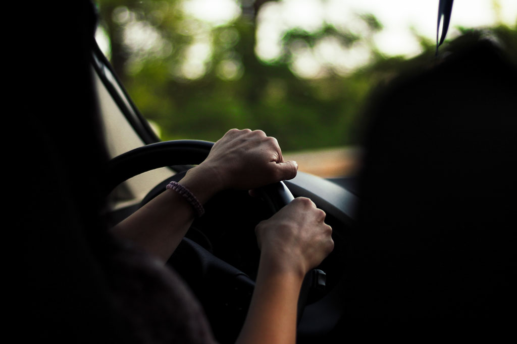 Person driving alongside greenery with both hands on the steering wheel