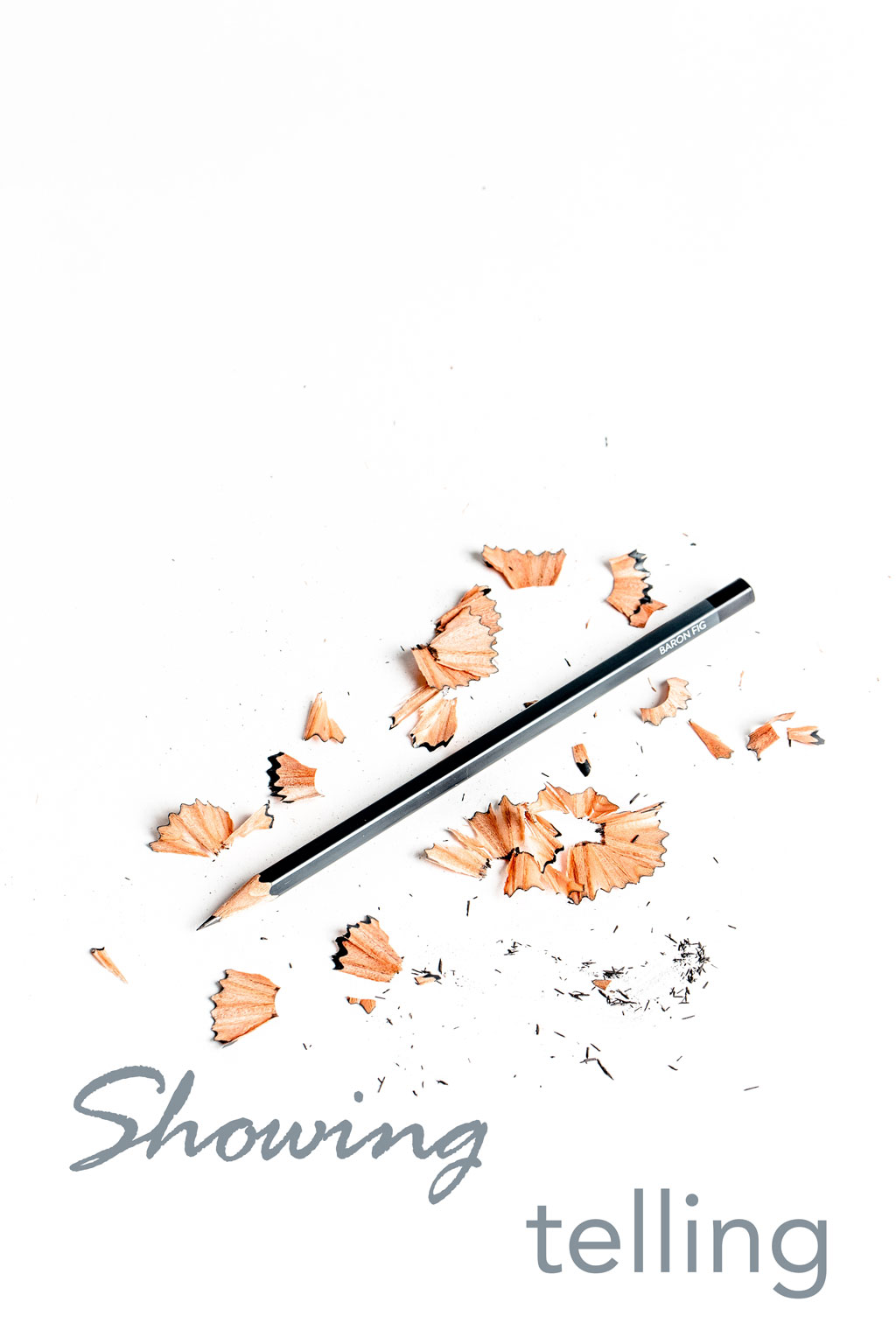 sharpened pencil lying amidst pencil shavings and text saying 'showing' and 'telling' on white background