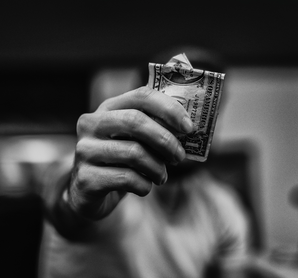 Black and white hand holding a crumpled dollar bill