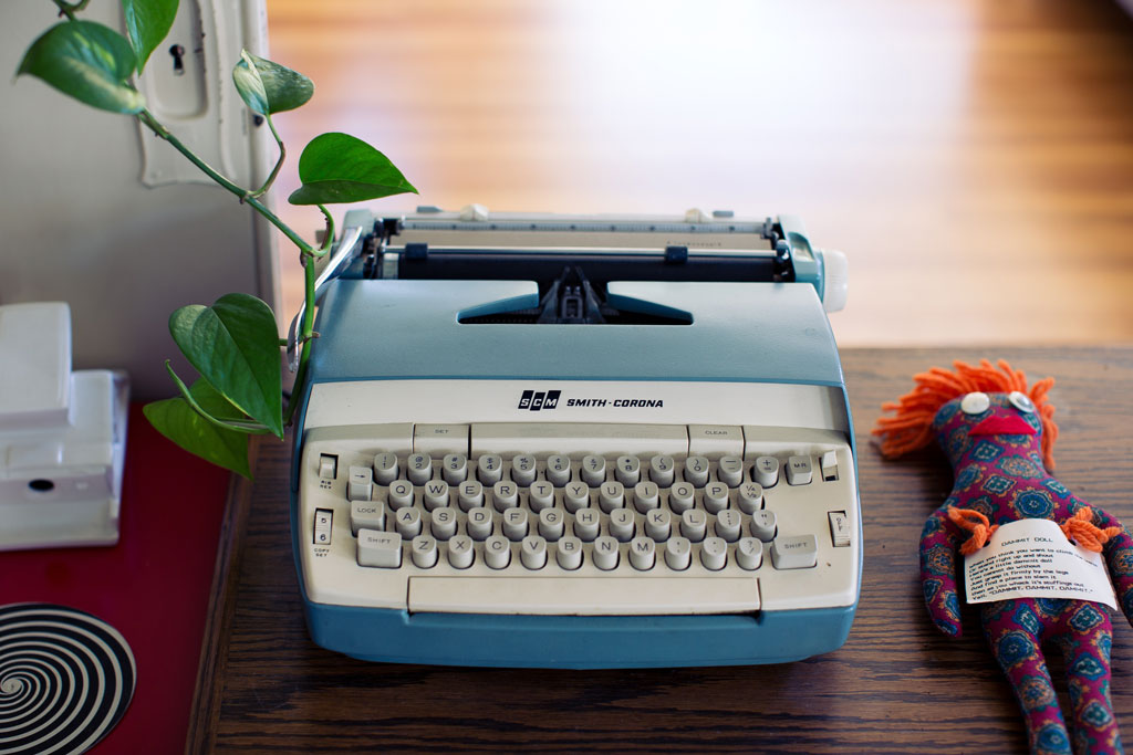 blue typewriter with cloth doll and plant on wooden desk