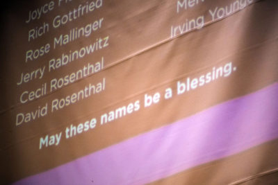 Overhead projection of victims' names with the phrase "May these names be a blessing."