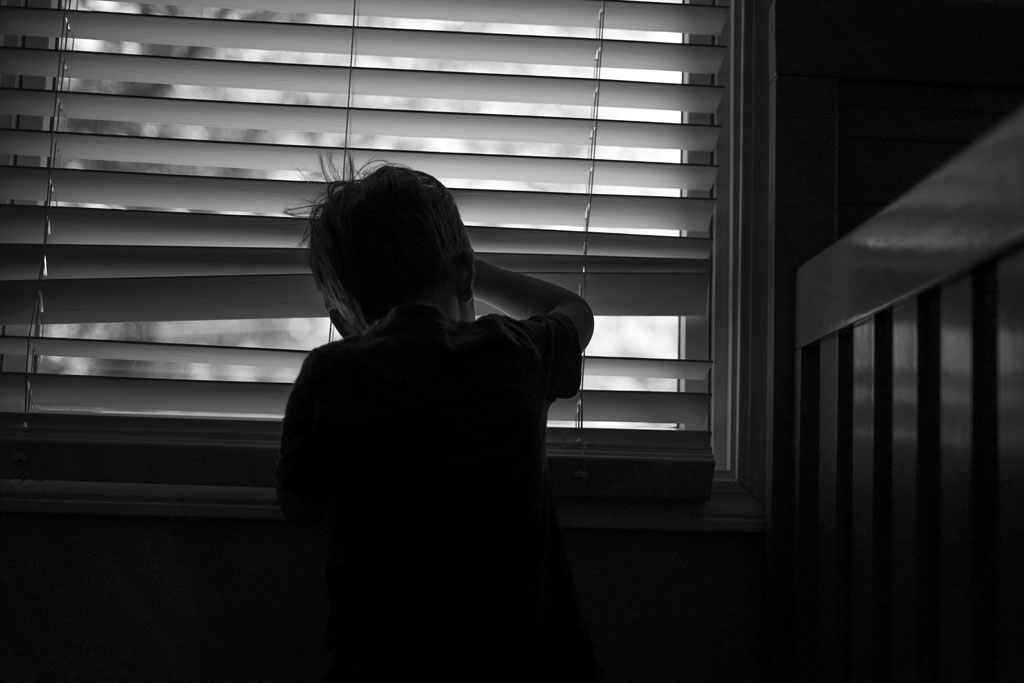 small boy peeking through a window to the outdoors