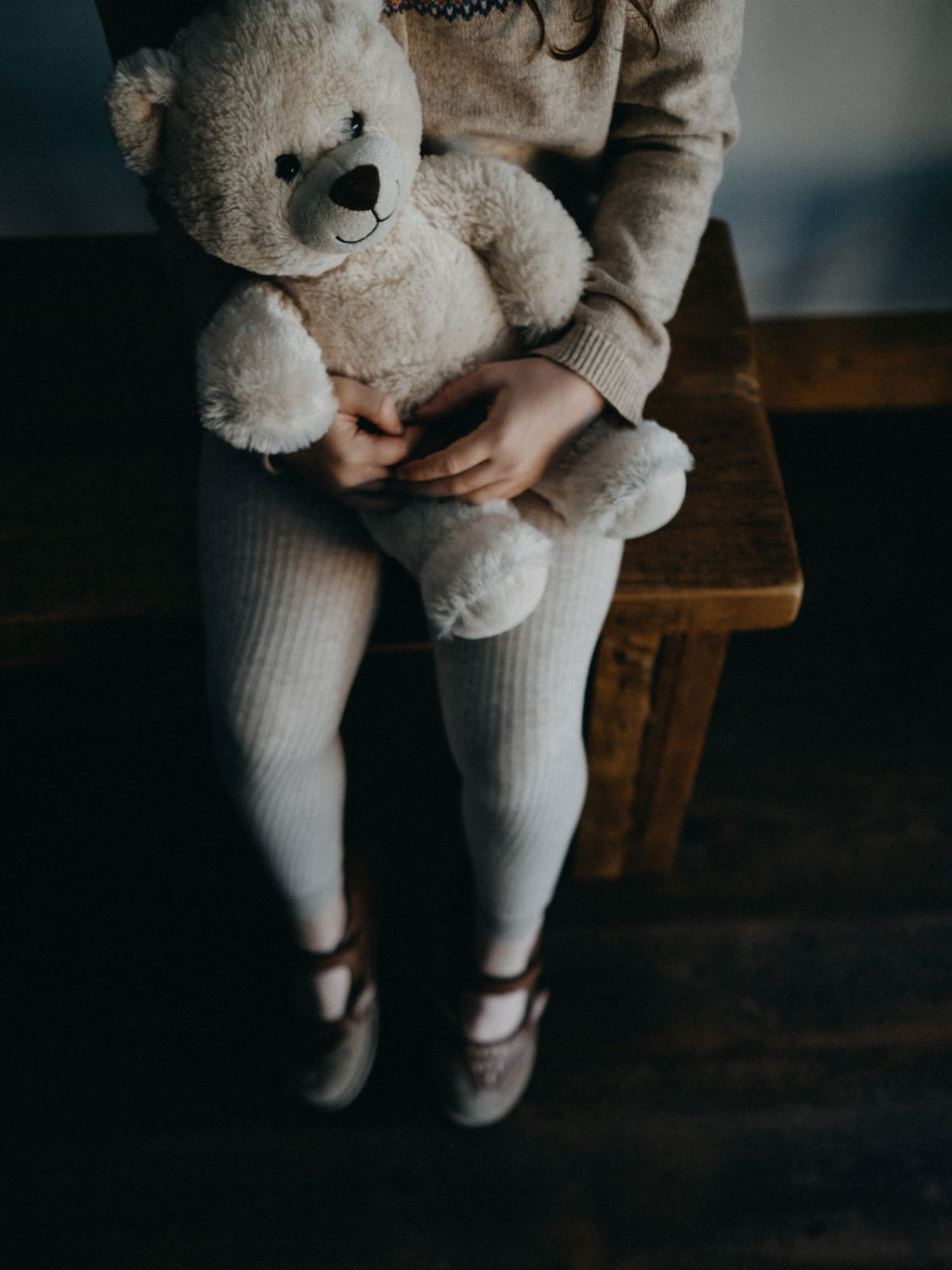 close-up of girl dressed in neutral colors holding white teddy bear